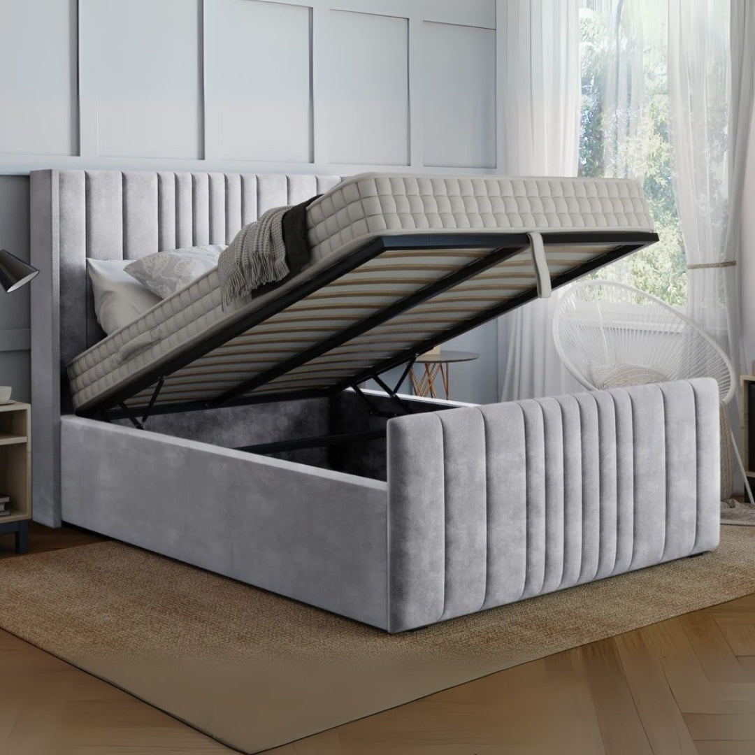 Gray upholstered bed with open storage compartment in a room with a window and curtains.

